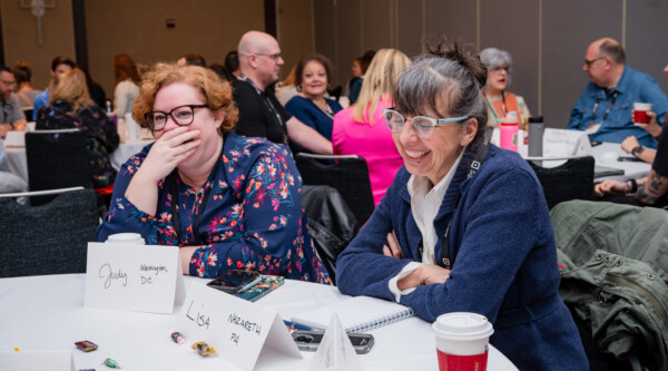 Two women sitting at a table laugh during a conference session