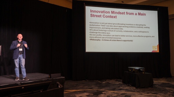 Matt Wagner speaking on a stage next to a powerpoint slide about innovation for Main Streets