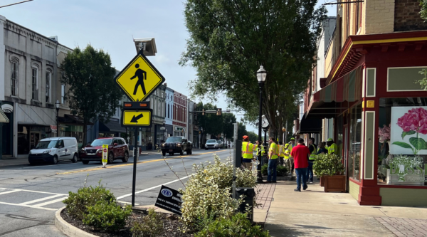 An intersection in a downtown district. Men are working on a project wearing high-visibility vests.