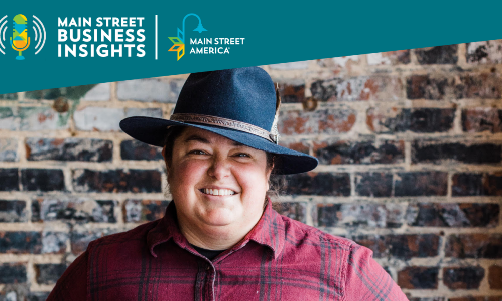 Smiling woman wearing hat and flannel shirt stands in front of brick wall