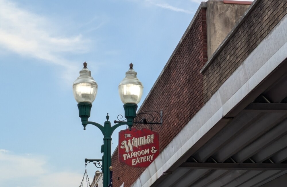 Exterior signage outside of a brick building. Sign hanging on light post reads, "The Wrigley Taproom & Eatery"