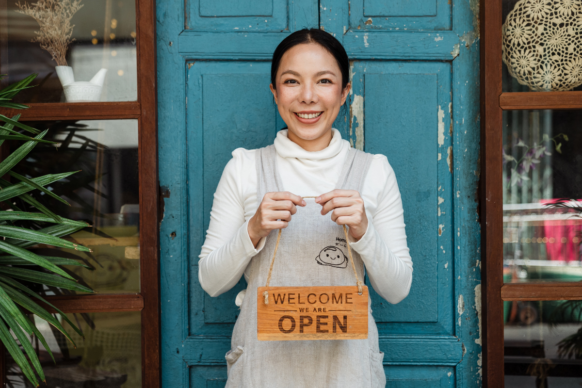 Woman holding sign called "Welcome We Are Open" in front of door