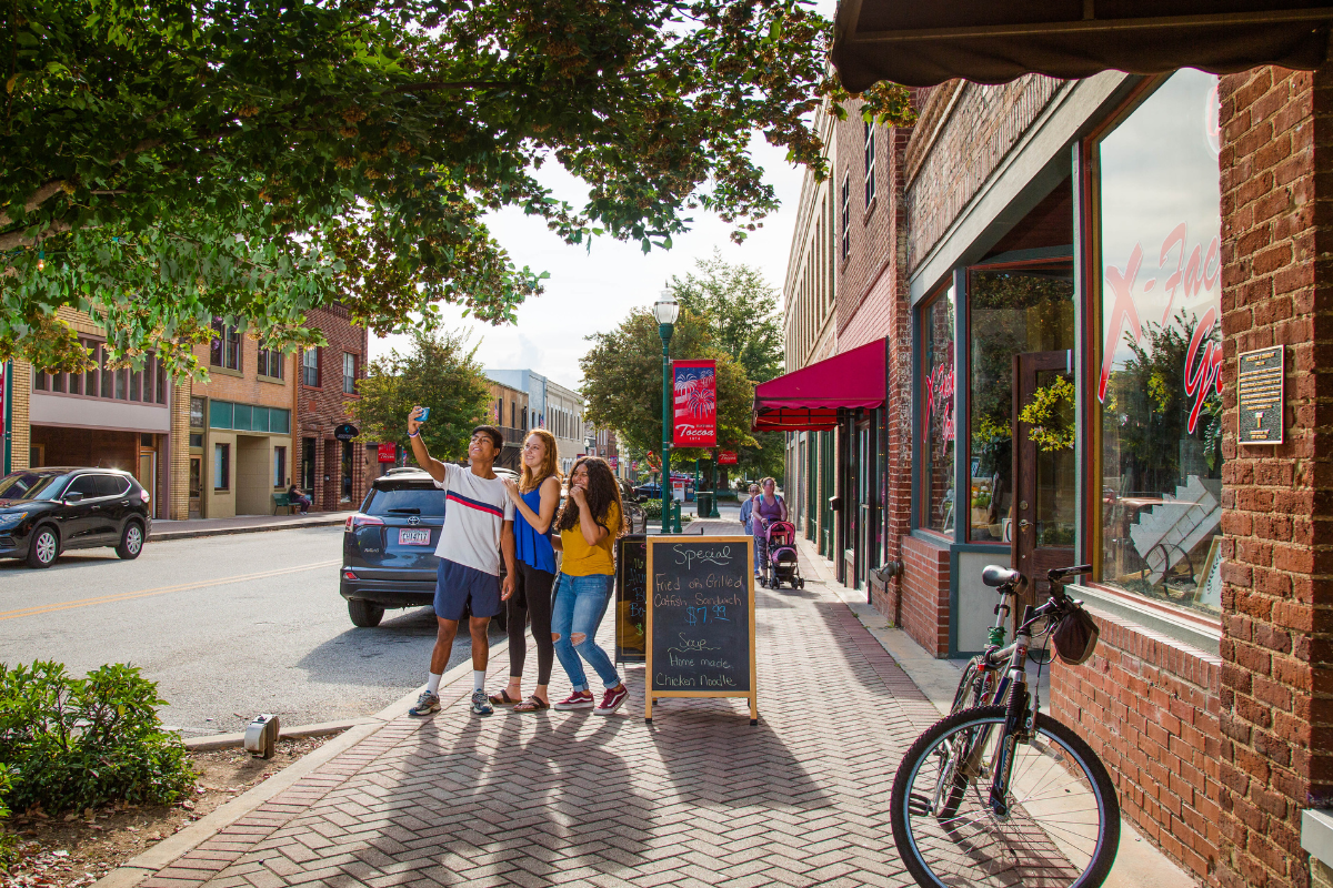 Group of three young people take a selfie in front of a downtown business.