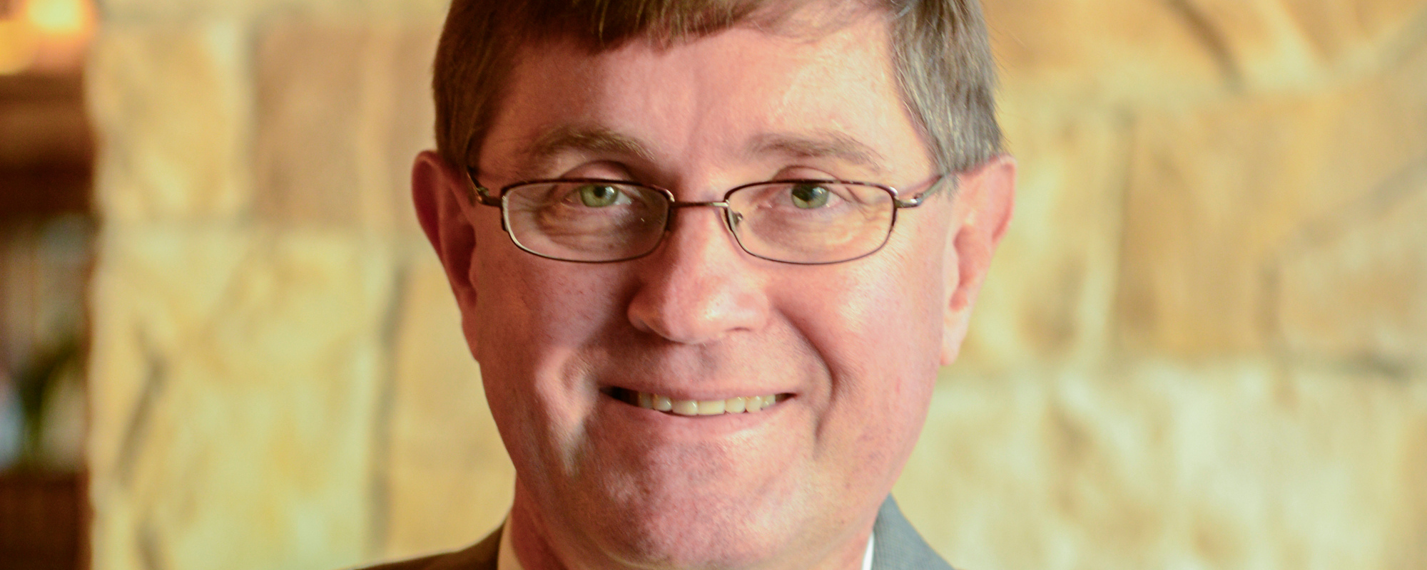 Headshot of man wearing glasses and gray suit.