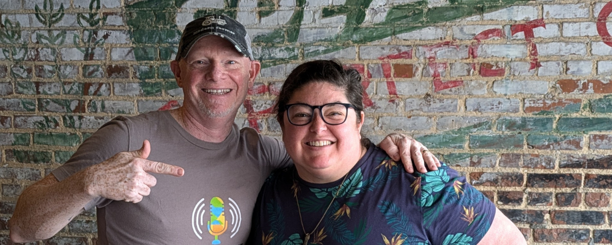 Man and woman smile in front of brick wall.