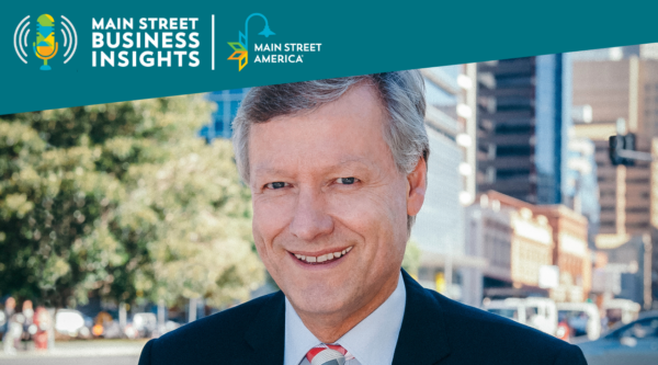 Headshot of man wearing black suit with tie in front of city scene