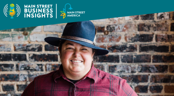 Smiling woman wearing hat and flannel shirt stands in front of brick wall