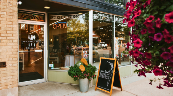 Storefront of the Carrot Seed with large windows, a sandwich board sign, and flowers