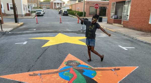Una joven artista posa detrás de su mural callejero Juneteenth