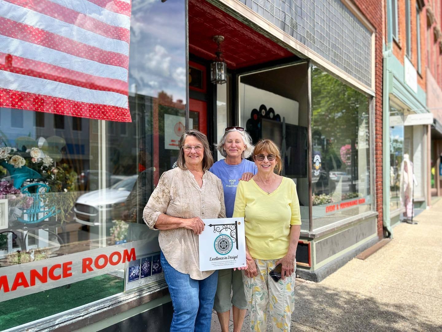 Three women standing in front of a storefront holding an award.