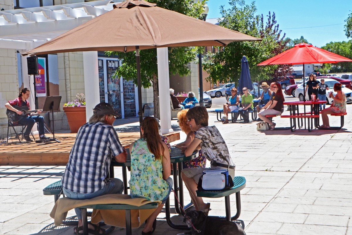 A musician plays the guitar to audiences of people gathered around picnic tables.