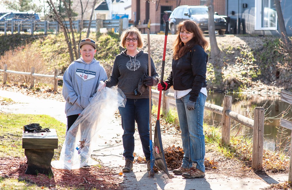 Two women and a young boy rake leaves in a park.
