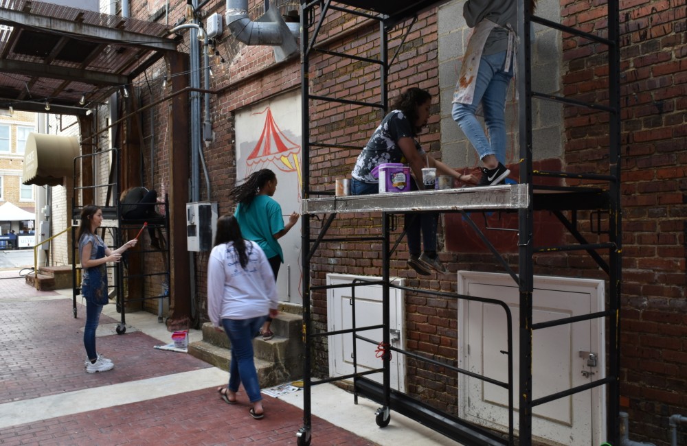 Young people paint a mural onto a brick wall.