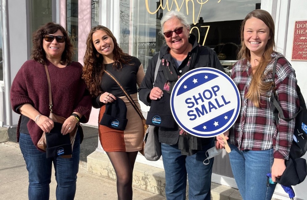 Women stand outside of a retail shop during a shop small event.