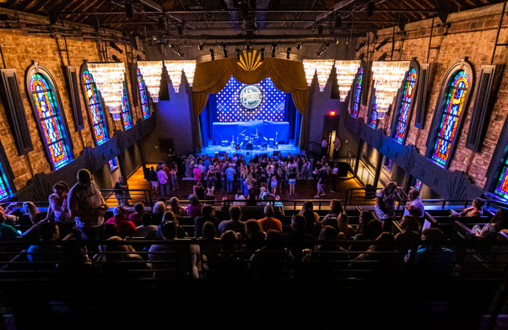 People are watching a music show in an old building that has stained glass windows.