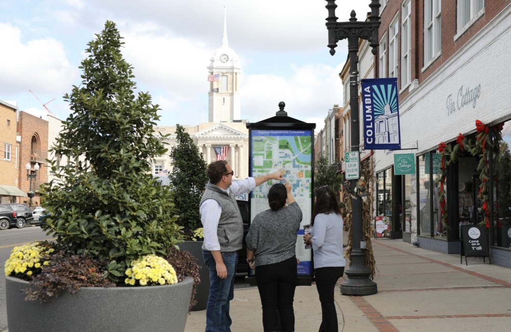 Three people are standing and looking at a directional map in a downtown area.