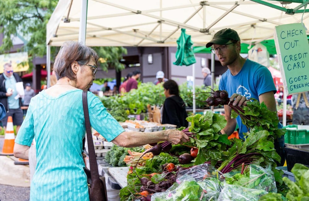 A person is looking at vegetables while a man is holding a vegetable under a large canopy tent outside.