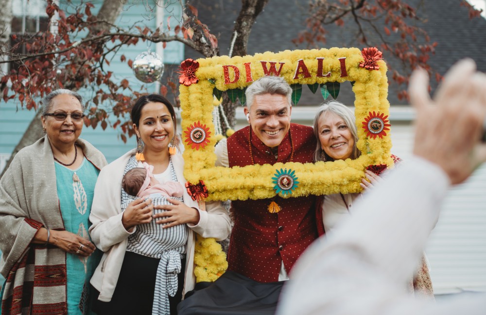 A group of people are smiling and two of them are holding a yellow sign that says "Diwali".