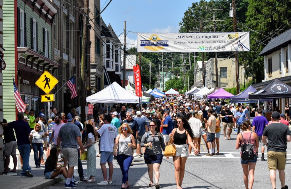 A large group of people are walking in the street with tents in the background.