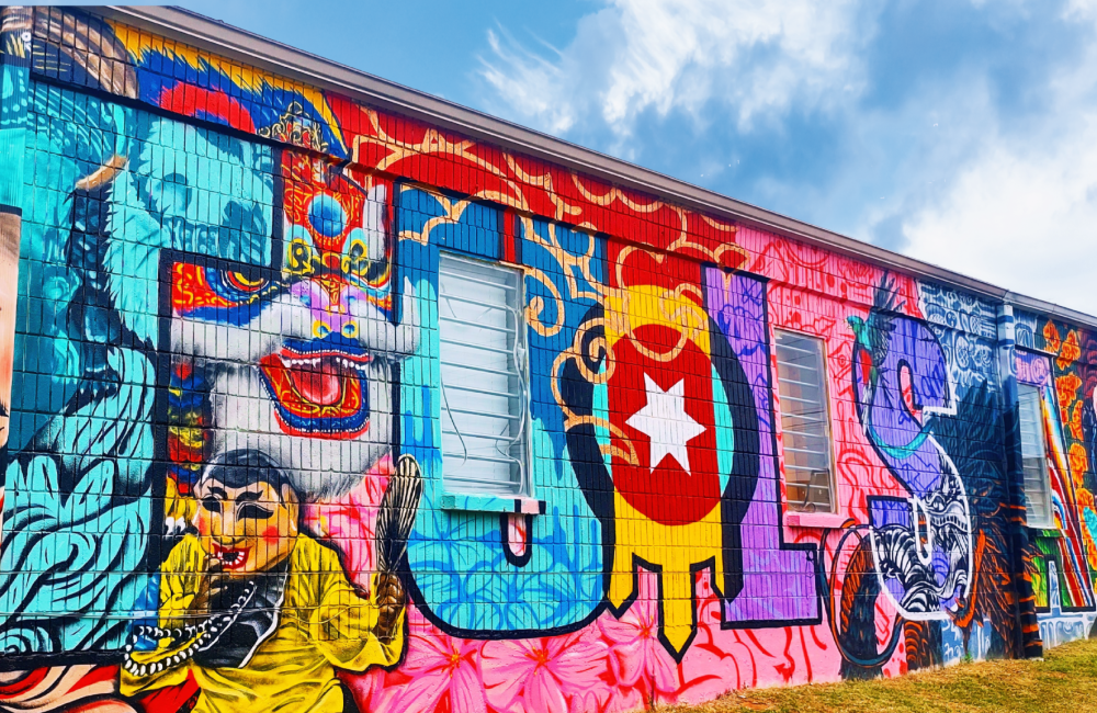 A brightly colorful mural painted on the side of a building that spells out the word "TULSA" in large, bold, stylized letters, each filled with distinct artistic elements and cultural imagery.