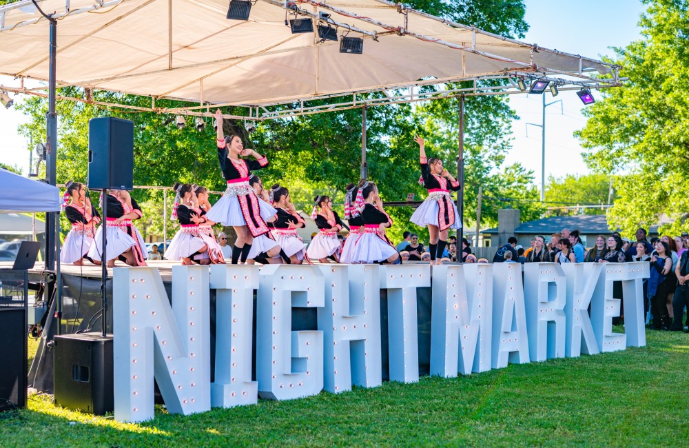 Performers dance on a stage outside with a big sign that reads "Night Market".