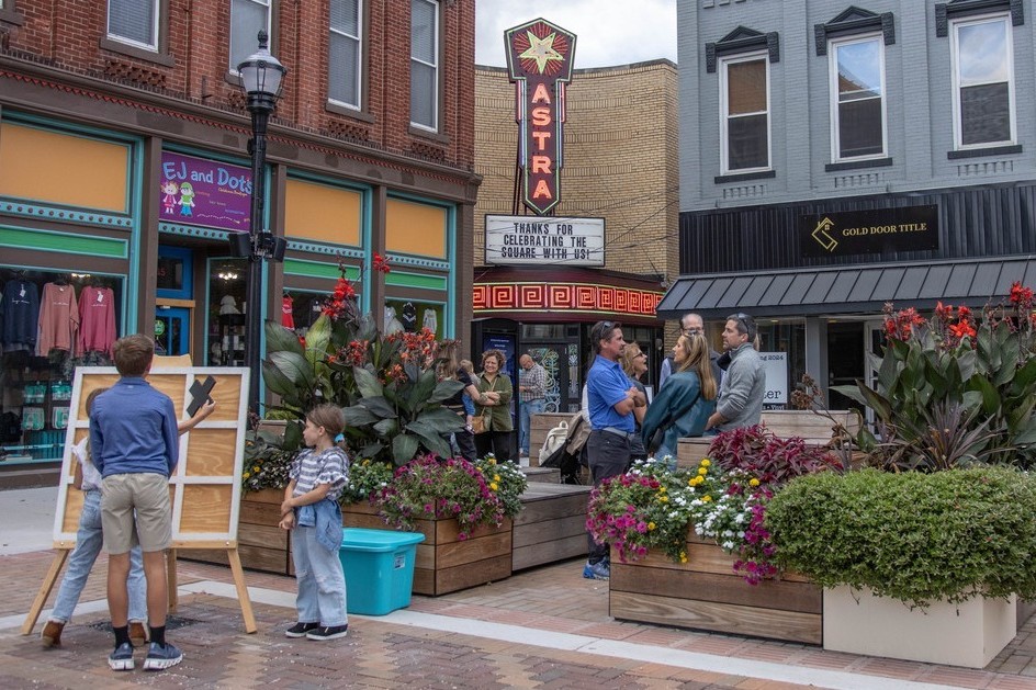 People gather in a town square surrounded by historic buildings.
