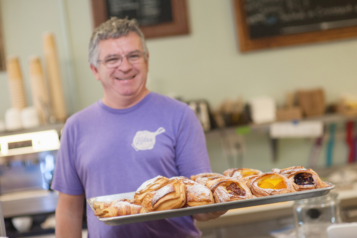 Man smiling while holding a tray filled with pastries.