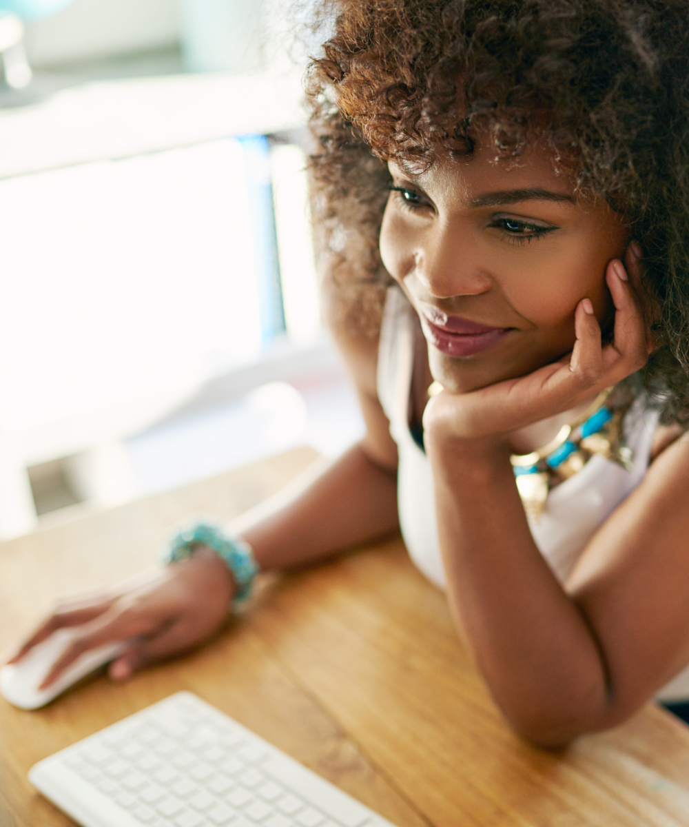 Image of black woman at computer resting left head on hand and with right hand on computer mouse