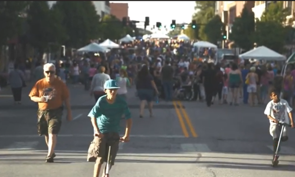 People walking and riding scooters at an outdoor street fair
