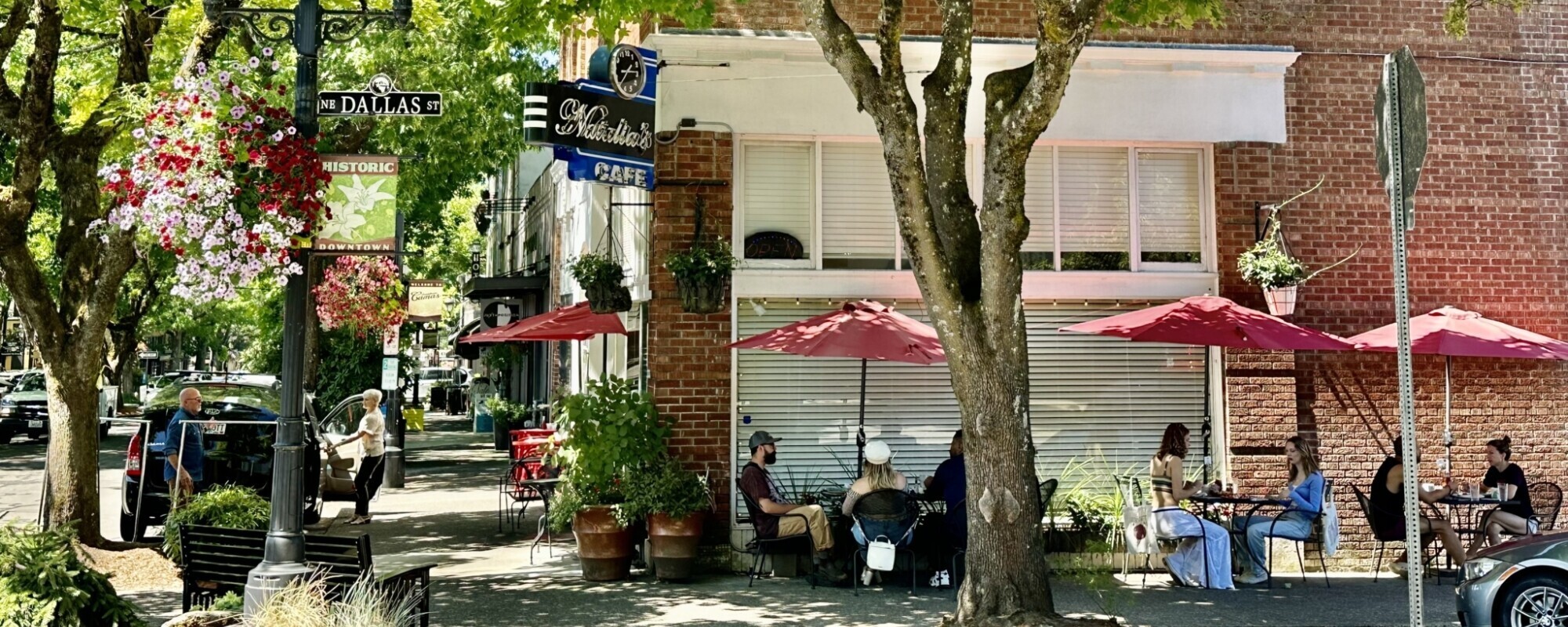 People enjoying outdoor dining under red umbrellas on a downtown street.