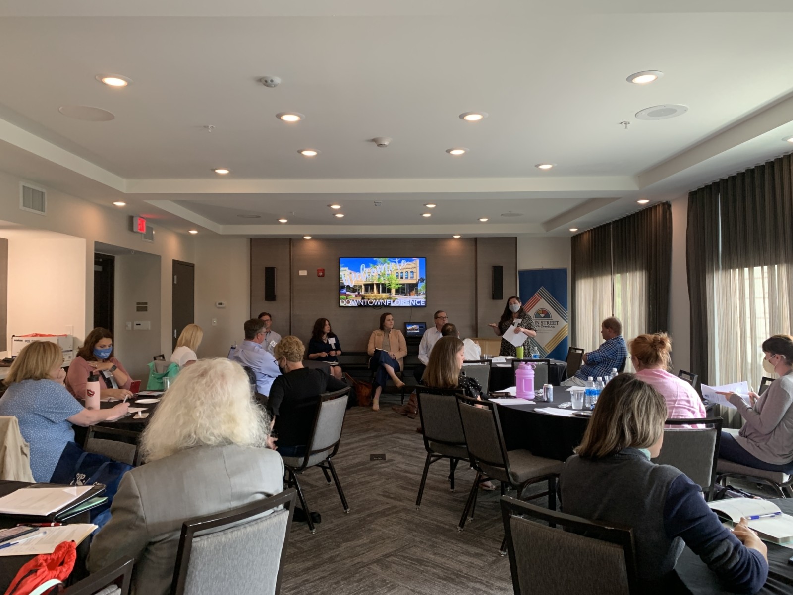 A room full of people sitting at tables listening to a presentation at a conference