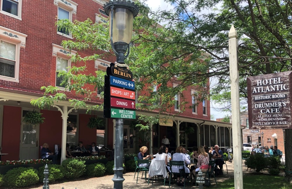 People sit around outdoor tables placed in front of a large, historic brick hotel.