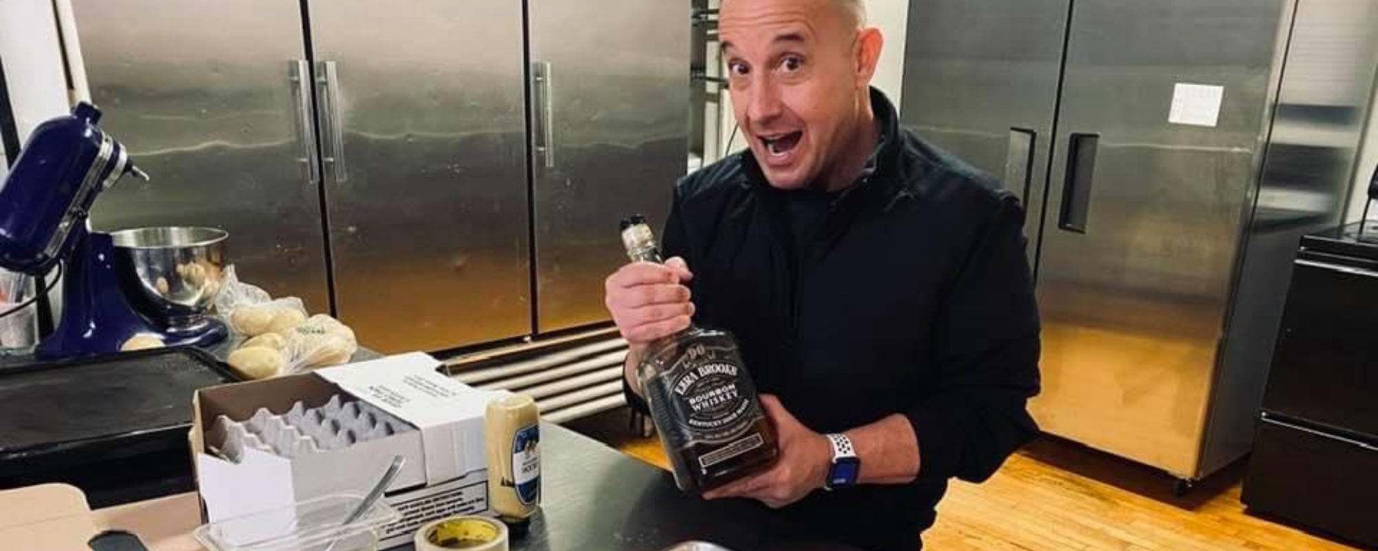 Man in industrial kitchen holds bottle of whiskey