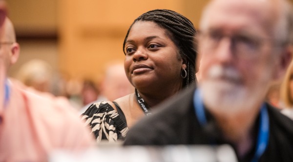 People listen intently to a speaker; in the center and in focus is a woman smiling.