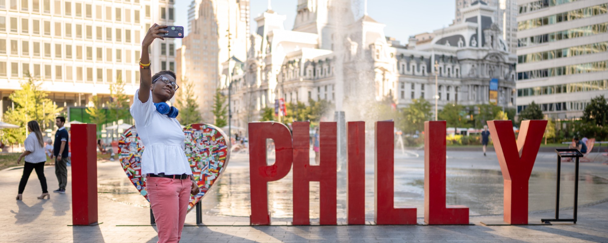 A woman poses for a selfie in front of large letters saying "I <3 Philly"