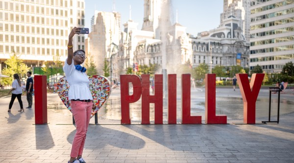 A woman poses for a selfie in front of large letters saying "I <3 Philly"