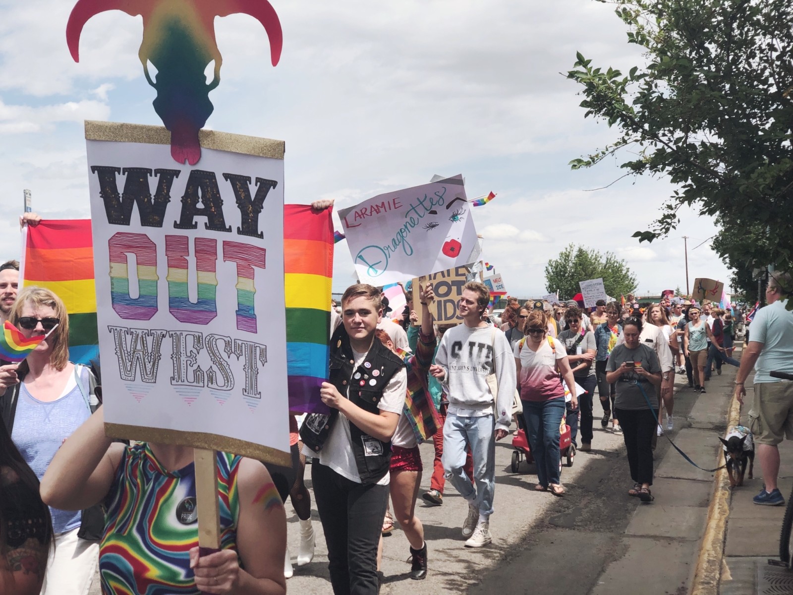 People marching in a Pride parade carrying a sign saying "Way Out West" and "Laramie Dragonettes"