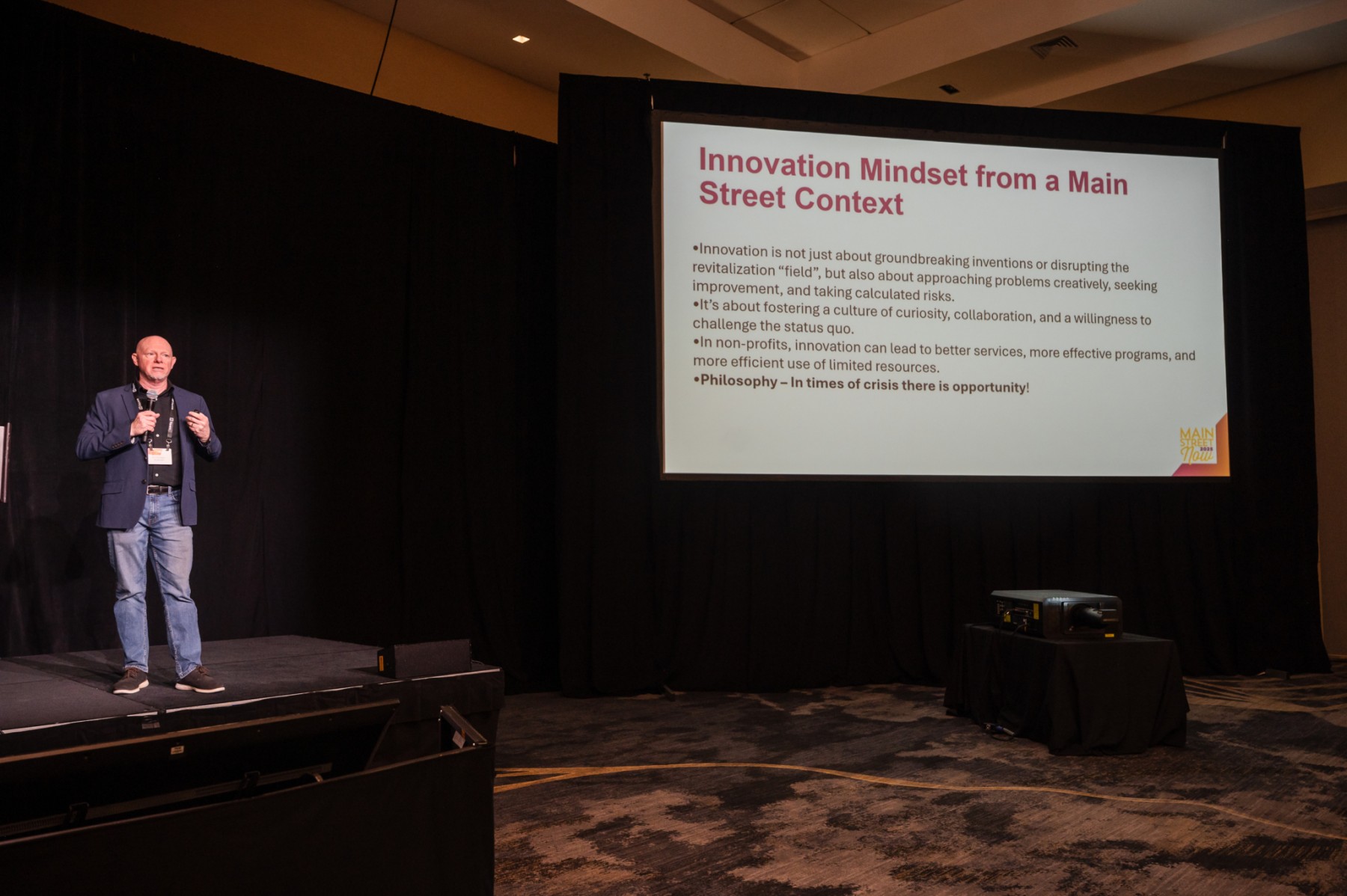 Matt Wagner speaking on a stage next to a powerpoint slide about innovation for Main Streets