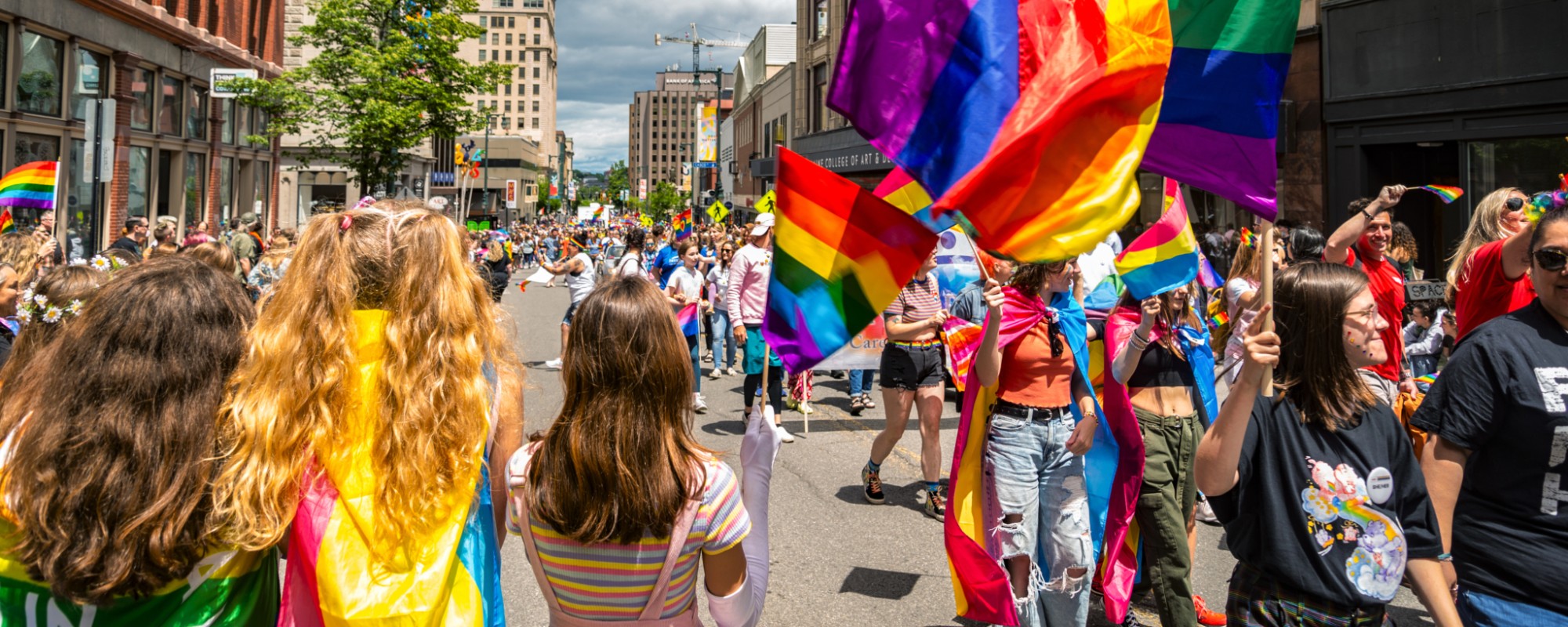 A group of people in colorful clothing carrying rainbow flags march in a Pride parade