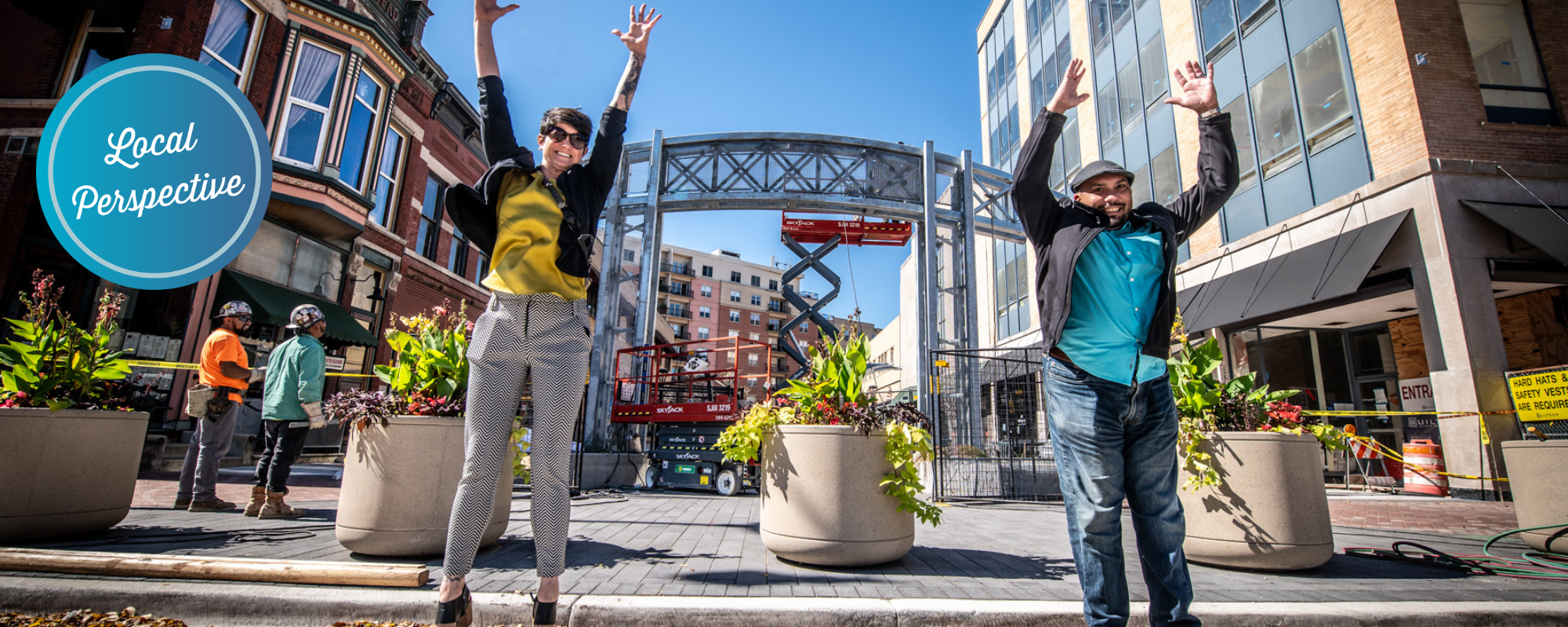 Two people jumping in the air on a downtown street. Sticker text in the corner reads "local perspectives"