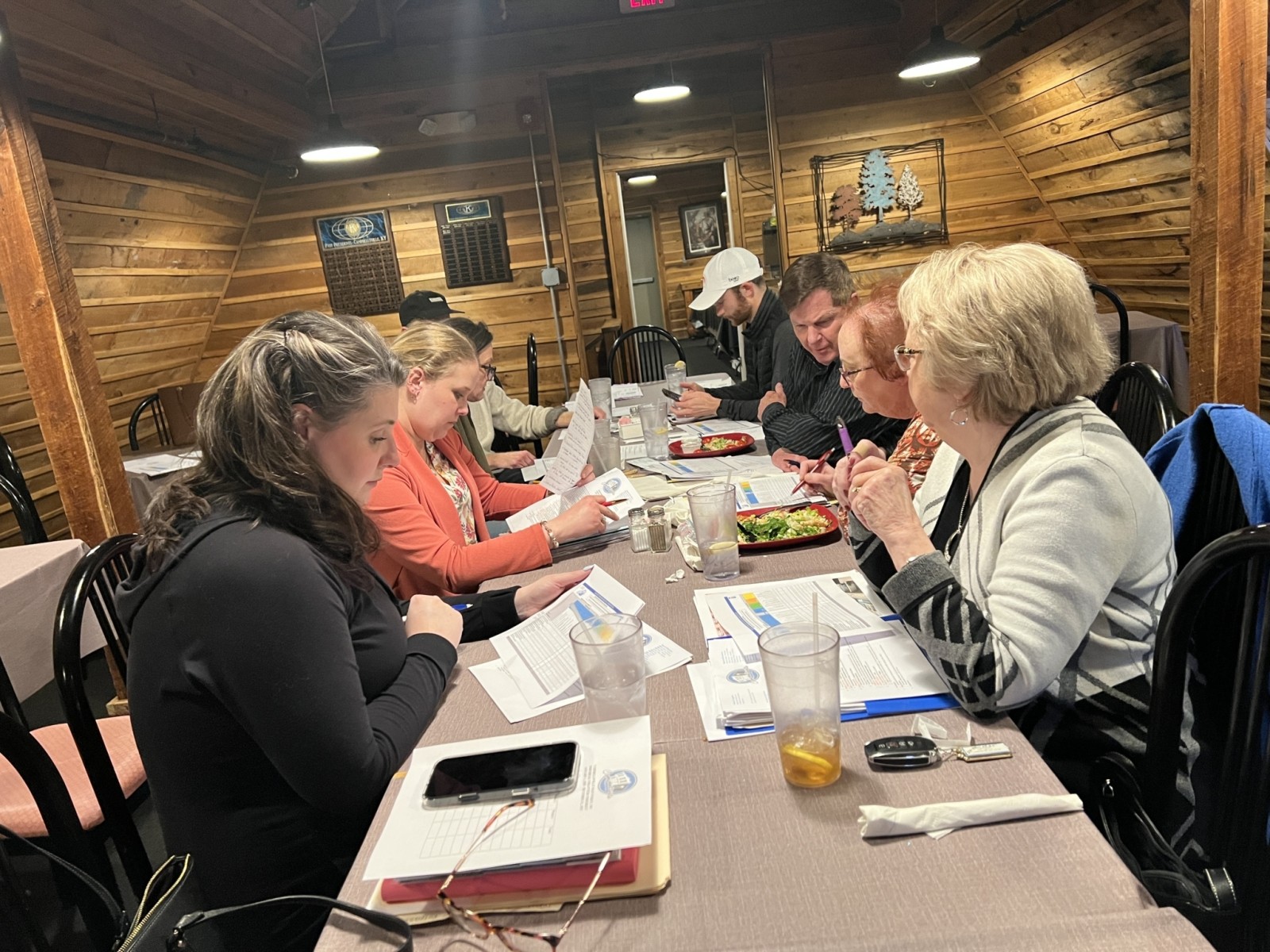 A group of people sit at a long table, looking at papers and discussing ideas