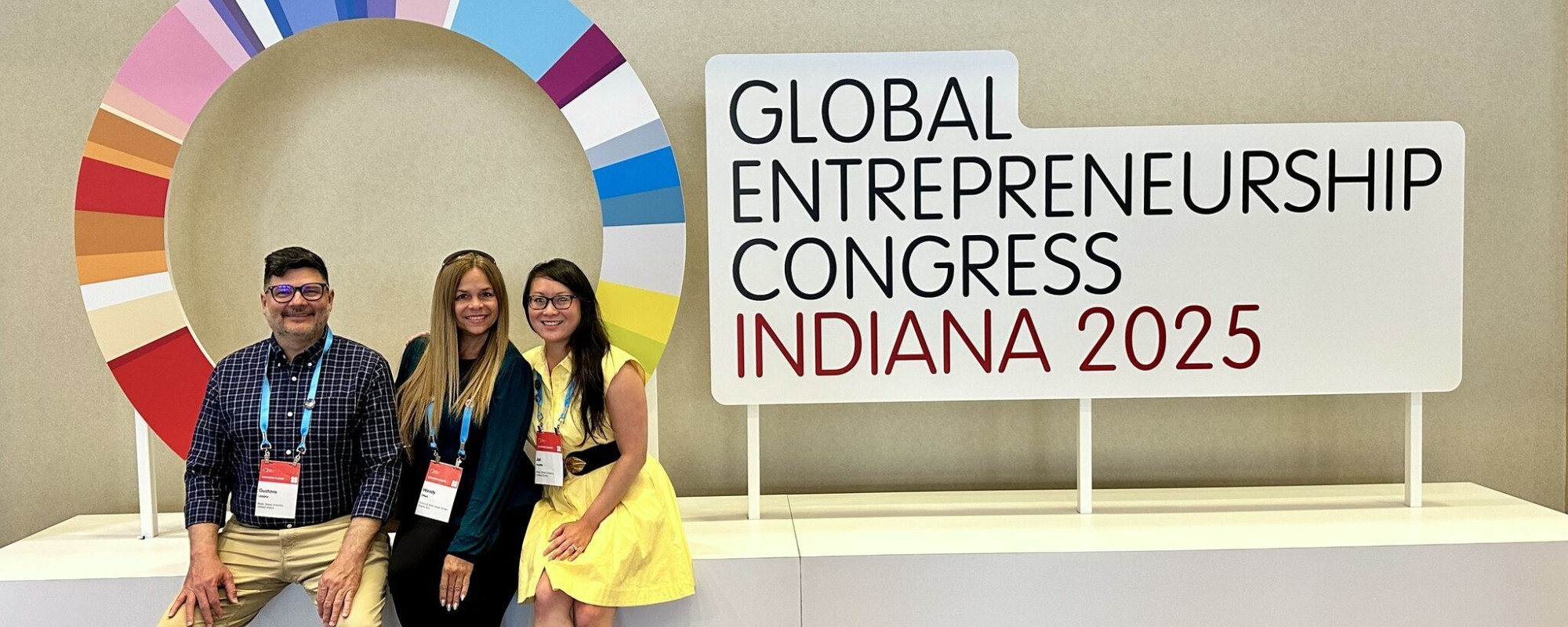 A man and two women pose in front of a sign with the logo for the 2025 global entrepreneurship congress.