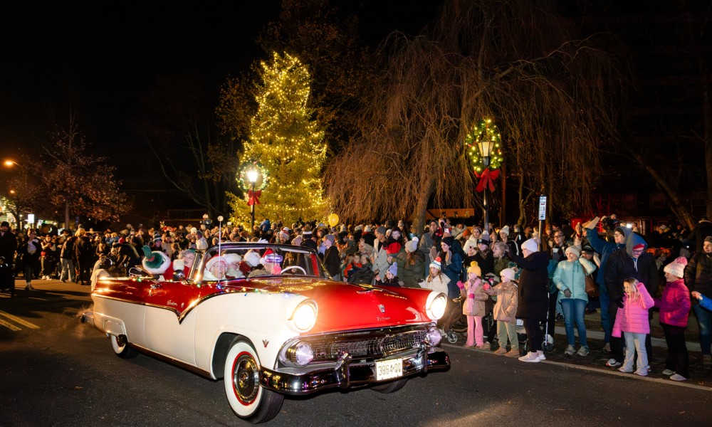 A red and white vintage car drives down a decorated street in a holiday parade