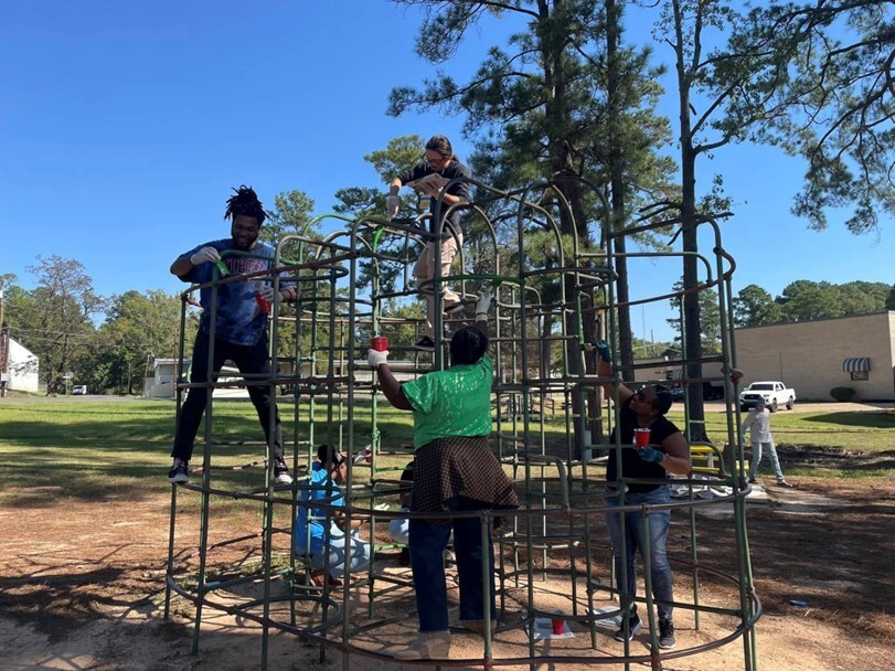 Volunteers climb on a play structure to apply paint