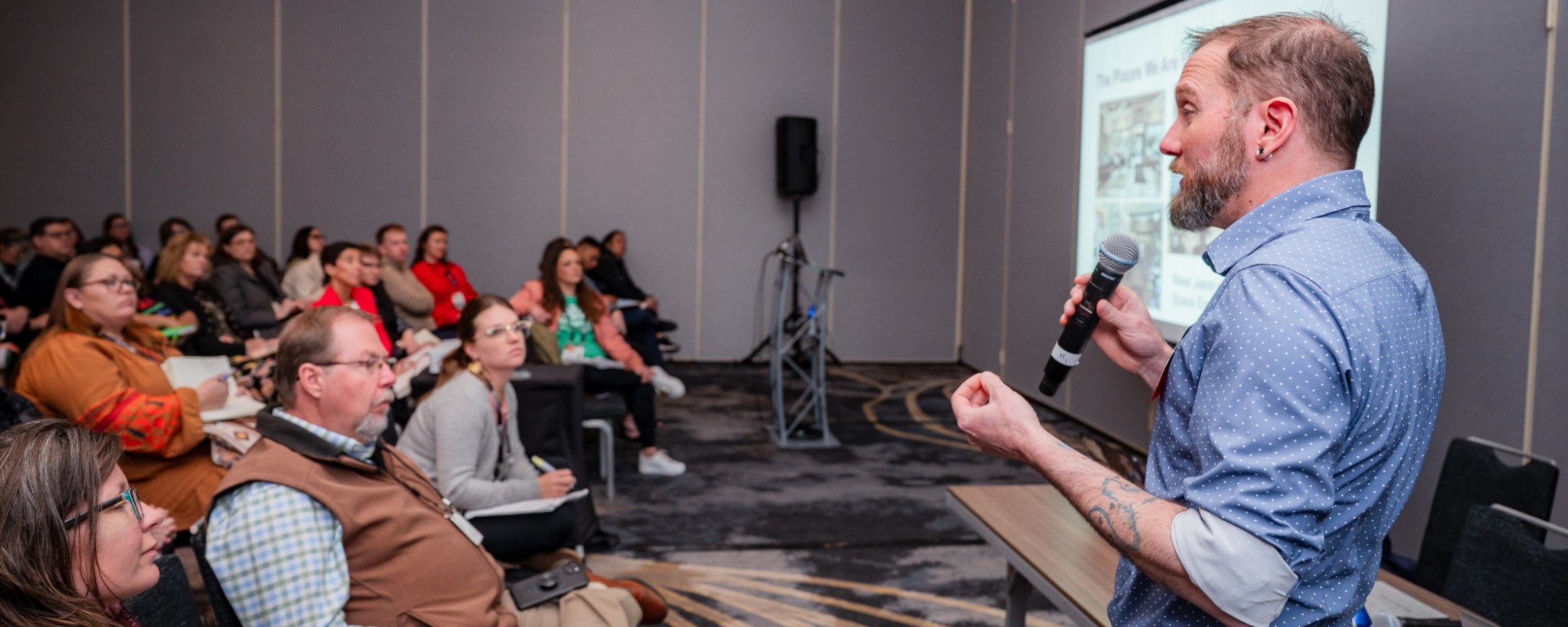 A man speaks to a large audience of people listening intently.