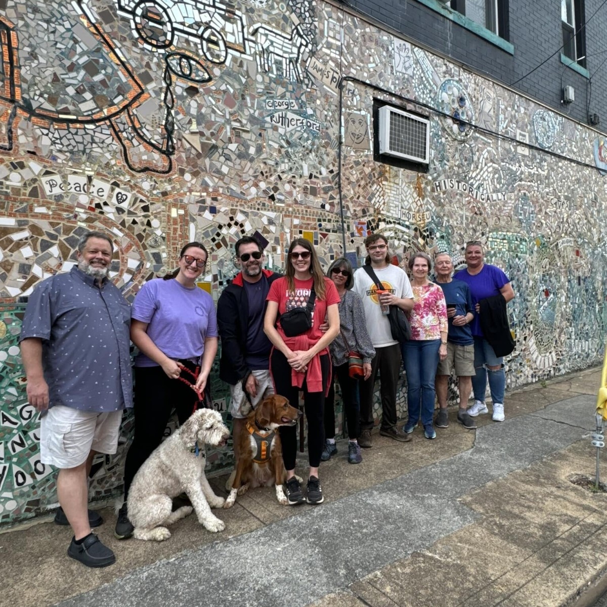 Small group of people pose in front of a mural