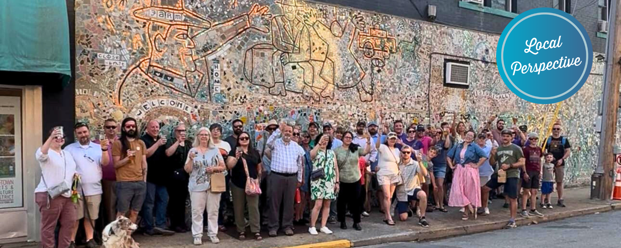 A large group of people pose in front of a mural