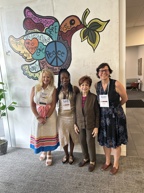 Four women stand in front of a mural depicting a peace dove.