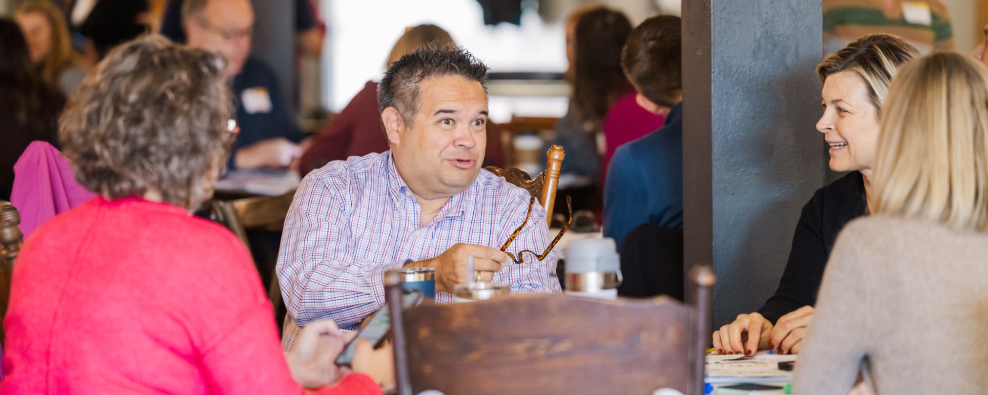 People sit around a table; in the center, a man gestures while speaking.