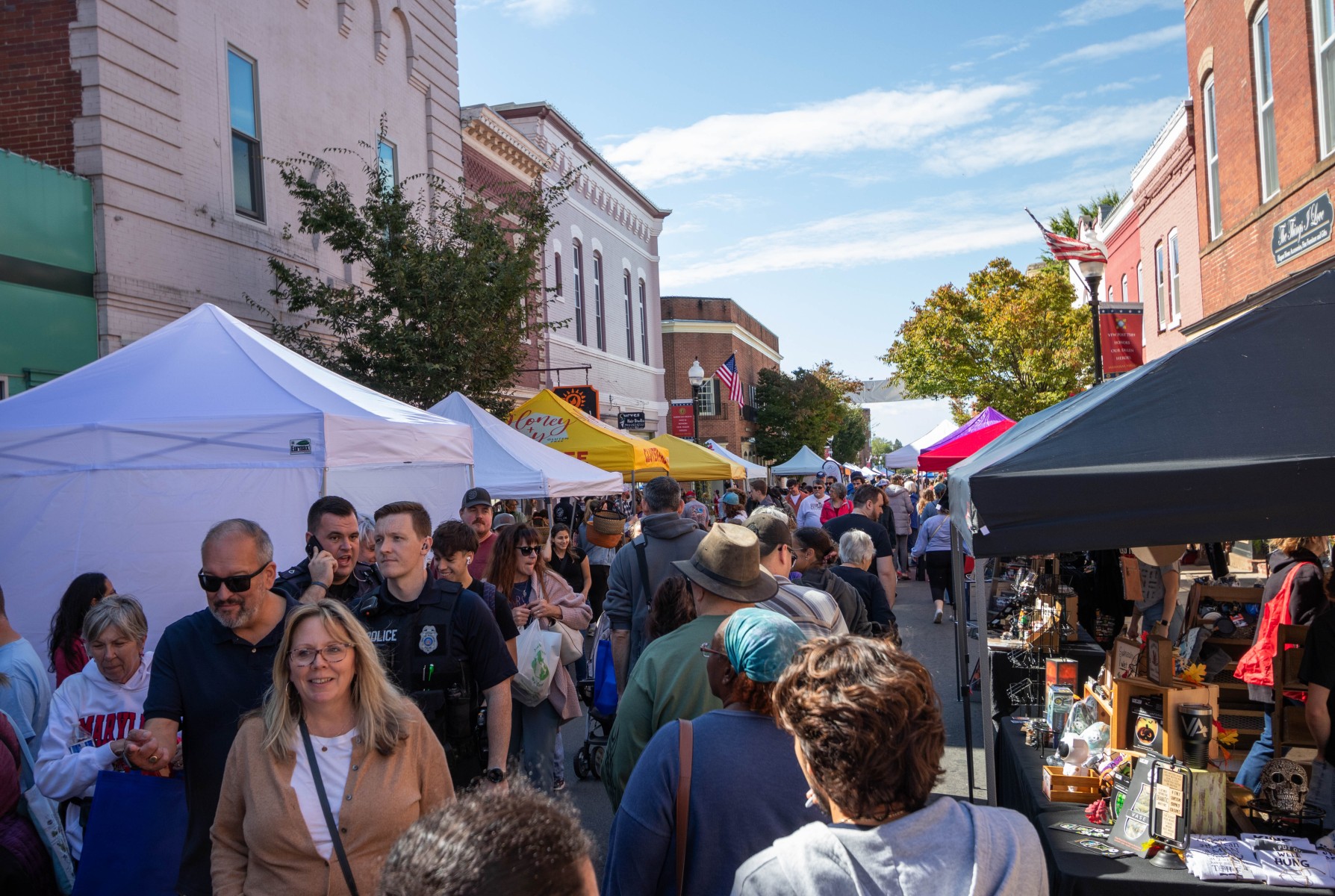 Crowds of people navigate vendor tents during a fall festival on a sunny day